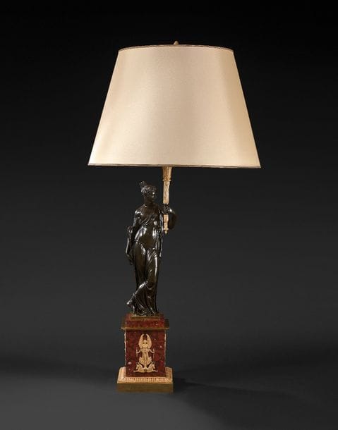 Grand flambeau en bronze patiné et bronze doré représentant une femme drapée à l’Antique tenant un brandon, reposant sur un socle de marbre rouge griotte à décor de caducée et figures de Victoire. ; (monté en lampe).
Époque Restauration, vers 1830.
H : 70 cm
