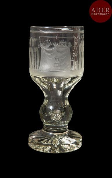 Verre dit « Canon » maçonnique en verre taillé gravé, cylindrique, sur pied travaillé de losanges, oves, pans coupés, fond étoilé, gravé à décors symboliques, branches d’acacias, croix, outils, gravé dans un triangle flamboyant, épées croisées, compas, plumes croisées. 
Hauteur. : 19 cm
B.E XXe siècle