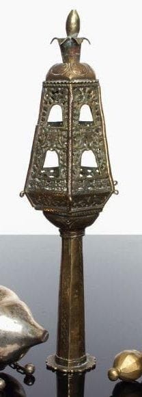 RIMON (seul, d'une paire)
Bronze ajouré et laiton gravé. Le pied octogonal, gravé d'un décor géométrique alternant avec des espaces lisses, est surmonté d'un corps hexagonal percé de deux étages de fenêtres se terminant par une prise en forme de fruits à couronne. Décor floral stylisé autour des fenêtres. Afrique du Nord (Maroc ?), XVIII ème-XIX ème siècle. Haut.: 34 cm. Sans les grelots ni leurs chaînes.