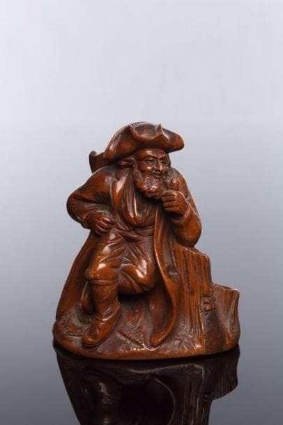 LE REPOS DU COLPORTEUR JUIF - Statuette porte pipes en buis tourné et sculpté représentant le colporteur, barbu et coiffé d'un tricorne, fumant sa pipe assis sur une souche, sa hotte sur le dos, en costume du XVIII ème siècle. Cette sculpture, d'une finesse remarquable (on identifie les dents dans la bouche et les papillotes devant les oreilles), représente, vu par un non-juif, un personnage typique des communautés juives de la vallée du Rhin, en particulier en Alsace, sans que l'on puisse, ce qui est exceptionnel à l'époque, y déceler la moindre trace de caricature ou d'antisémitisme. Vallée du Rhin, début du XIX ème siècle. Haut.: 14 cm.