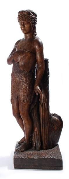 Curieuse sculpture en chêne d'un jeune homme, vêtu d'une peau de chameau, qui pourrait être Saint Jean-Baptiste.  Il est coiffé d'un bonnet de fourrure et tient de sa main gauche le haut de son vêtement. Il s'appuie contre un tronc d'arbre, sur sa partie arrière, le tout reposant sur un socle. France, XVIIIe siècle. Hauteur : 108 cm. Accidents et manques.