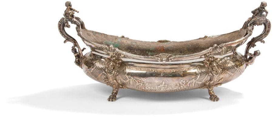 Jardinière en argent (950 ‰) et sa doublure amovible en zinc, de forme ovale, elle repose sur quatre pieds griffe à attaches de mascarons dans des médaillons feuillagés. Le corps est repoussé de larges cartouches fleuris dans des encadrements de croisillons. Sur chaque prise à enroulements figurent deux putti en fondu ciselé.
Poinçon minerve
Orfèvre : Henri SOUFFLOT 1884 - 1910
Poids net : 2035 g - longueur : 44,5 cm - largeur : 26 cm - hauteur : 9,6 cm