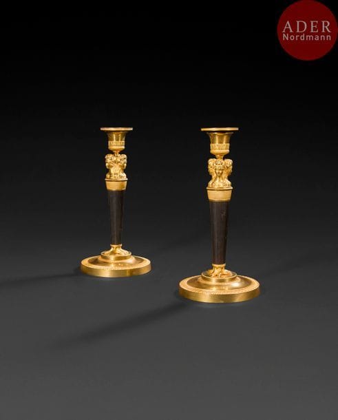 Paire de flambeaux en bronze patiné et bronze doré, le fût à pans surmonté de bustes de femmes reposant sur des pieds féminins et une base circulaire à emmarchement et décor de feuilles d’eau.
Époque Consulat, vers 1800.
H : 25 cm
