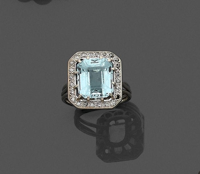 Bague en fils d’or gris 18K (750), ornée d’une aigue-marine taillée à pans dans un entourage de diamants ronds. 
Tour de doigt : 54. 
Poids brut : 6,5 g (manque)