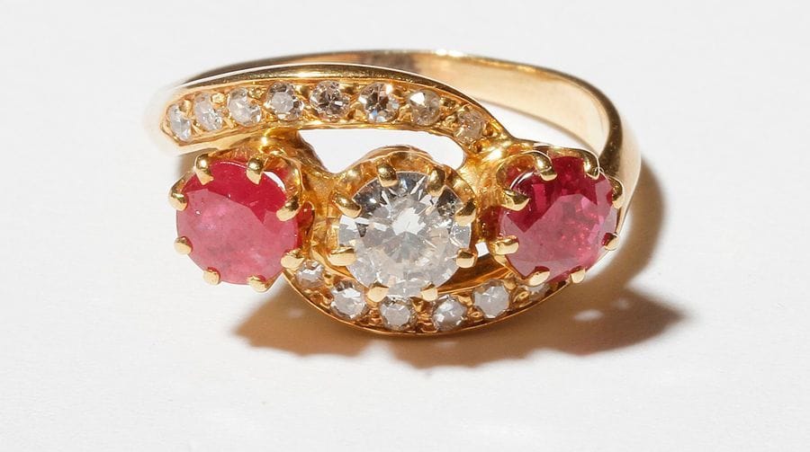 Bague en or 18K (750), ornée d’un diamant rond entre deux rubis et deux courbes de diamants. Tour de doigt : 50. 
Poids brut : 4 g