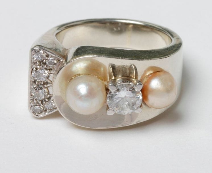Bague assymétrique en or gris 18K (750) et platine ornée d'un diamant rond entre deux perles de culture et diamants ronds plus petits. Travail des années 40. 
Poids brut : 9,7 g