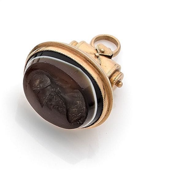 Pendentif-sceau en or 18K (750), orné d’une intaille en verre représentant un personnage casqué de profil. Travail de la seconde moitié du XIXe siècle. 
Poids brut : 16,7 g