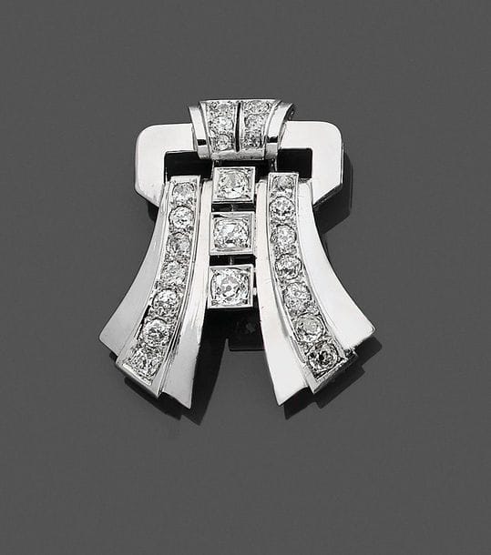 Broche-clip en or gris 18K (750) formant un motif géométrique serti de diamants ronds. Travail des années 1940. 
Hauteur : 4,1 cm environ.
Poids brut : 16,3 g