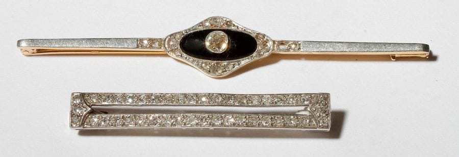 Lot de deux broches : la 1er en platine et or gris 18K (750), ornée d’un onyx, de diamants de taille ancienne et de diamants taillés en roses ; la 2e en platine agrémentée de diamants taillés en roses. Travail des années 1930. Longueurs : 7,4 et 4,5 cm environ. 
Poids brut : 10,5 g