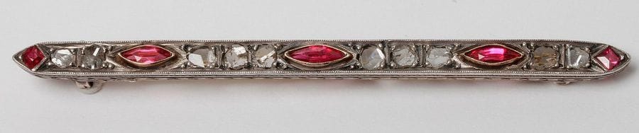 Broche-barrette en or 18K (750), sertie de diamants taillés en roses plates et de pâtes de verre rouge. Travail des années 1930. Longueur : 7,7 cm environ. 
Poids brut : 6,9 g (égrisures)