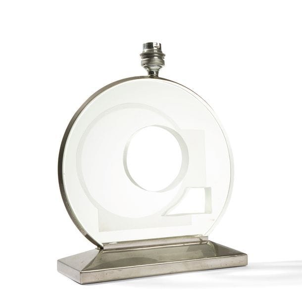 TRAVAIL MODERNISTE DES ANNÉES 1930
Rare et intéressant pied de lampe.
La base en métal nickelé accueille un épais disque de verre, maintenu par un jonc circulaire également nickelé, percé d’un cercle et d’un rectangle et au décor géométrique profondément gravé au jet de sable.
Deux petits éclats de surface dans la partie du disque maintenue par la base.
Hauteur avec douille : 29 cm
Longueur : 22 cm