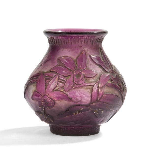 BURGUN – SCHVERER & CIE (VERRERIE D’ART DE LORRAINE – MEISENTHAL) 
Orchidée Cattleya
Vase piriforme à col évasé reposant sur un talon (anciennement accueilli par la base en métal).
Épreuve en verre, teinté mauve dans la masse, au décor dégagé à l’acide et rehaussé de dorure.
La partie sans motifs floraux est entièrement repris à la roue façon martelage.
Circa 1895/1900.
Manque la base en métal, dorure dans le décor altérée.
Porte la marque à l’or Verrerie d’Art de Lorraine et du monogramme B. S. C. avec la mention Déposé sous la base.
Hauteur :  8 cm