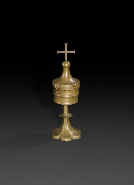 Ciboire en bronze à patine naturelle. Boîte tournée et moulurée, destinée à recevoir une pyxide, surmontée d’un couvercle conique couronné d’une croix?; tige hexagonale au nœud aplati reposant sur une base polylobée?; croix démontable fixée par un pas de vis.
Allemagne, XV / XVIe siècle. 
H?: 31,3?cm 