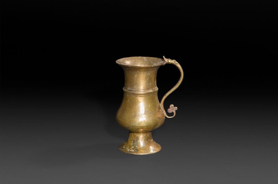 Aiguière en bronze. Corps tourné en balustre souligné par un filet?; anse serpentiforme avec attache en forme de tête de dragon et extrémité se terminant par un trèfle. Typologie Rare.
XVe siècle. 
H?: 16,8?cm, D?: 9,3?cm
(quelques accidents, traces d’oxydation et restaurations) 
 