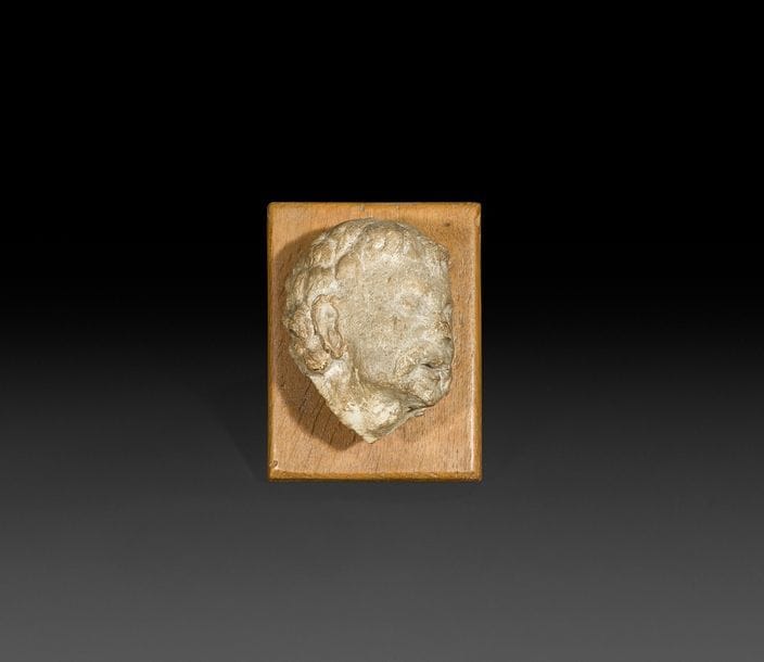 Tête d’homme moustachu en pierre calcaire sculptée. Les yeux clos, la bouche entrouverte.
XVe siècle
H?: 11,5?cm, L?: 8,7?cm
Soclée sur une planche de bois
(fragment, accident au nez) 