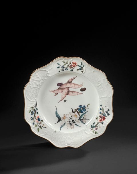 MEISSEN
Assiette en porcelaine à bord contourné du service « Brühlsche Allerlei », l’aile à décor en léger relief de motifs de vannerie et coquilles et de branches fleuries et au centre de fleurs de botanique et cosses de haricot.
Marquée épées croisées en bleu, C en pourpre et 21 en creux.
XVIIIe siècle, vers 1745-1746.
D : 26 cm

Provenance : 
Cette assiette provient du service commandé en 1742 par Heinrich Graf von Brühl et mentionné dans son inventaire après décès dans son Palais à Dresde en 1763. 

La marque C en pourpre indique que cette assiette était destinée à l’office ou Conditorei. 
Deux importantes parties du service sont passées en vente publique (Sotheby’s Londres, 8 juillet 1997, lot 57 et Sotheby’s New York, 21 novembre 2014, lot 1304).
Pour une étude du service, voir Johanna Lesmann, « Das Brühlsche Allerlei Ein Service für Heinrich Graf von Brühl », sous la direction de Ulrich Pietsch, Schwanenservice, 2000, pp. 106-123.