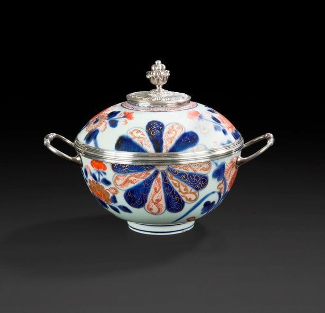 JAPON
Écuelle couverte en porcelaine à décor bleu, rouge et or Imari de rosaces et branches fleuries, prise du couvercle et anses en argent.
Poinçon de décharge de Paris 1717-1722.
XVIIIe siècle, vers 1720.
H : 16 cm, L : 21 cm, poids brut : 758 g
Léger enfoncement à la prise du couvercle.