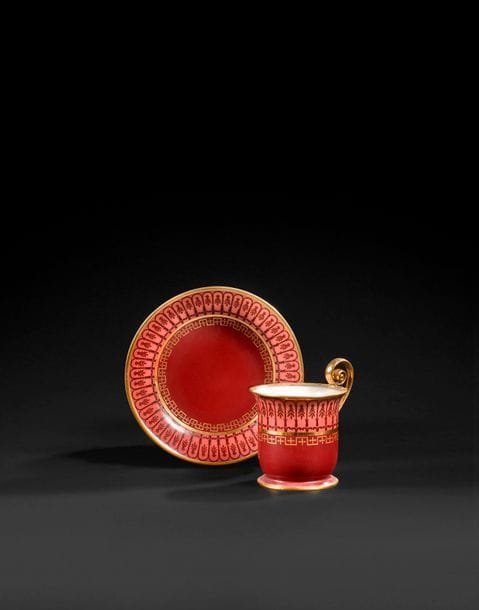 SèVRES 
Tasse à anse élevée et sa soucoupe en porcelaine dure nommée tasse calice à volute à décor en or et pourpre de frises de grecques, arcades et palmes sur fond rouge en deux tons.
Marqués en bleu LL entrelacés, fleur de lys et Sèvres et en or N 29 O 19, marque de peintre HL
Époque Restauration, année 1819.
H : 9,5 cm, D : 14 cm
(Anse recollée).

Provenance : 
Étiquette Nicolier au revers.