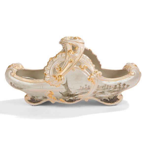 ÉMILE GALLÉ (1846-1904) 
Voiliers en bord de mer 
Jardinière de table de forme corbeille. Épreuve en faïence ajourée traitée dans le goût baroque, les palmettes et écailles traitées à l’or, le décor maritime double face traité façon grisaille. Cheveux épars. Marquée E. G. Croix de Lorraine déposé et Émile GALLÉ à Nancy sous la base. 
21 x 42 x 18 cm 