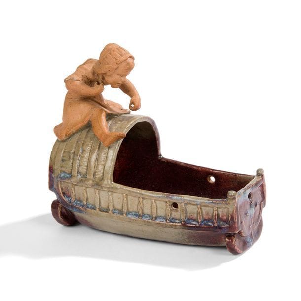 HENRI ROBALBHEN (1862-1906)
L’enfant au berceau 
Sujet décoratif pouvant former jardinière de table. Épreuve en grès émaillé sang-de-bœuf, céladon et bleu. L’enfant traité sans émail. Manque la cordelette et petits chocs épars. Signé ROBALBHEN Paris à la paix 34 avenue de l’Opéra sous la base. H.16,5 cm – L. 18 cm 