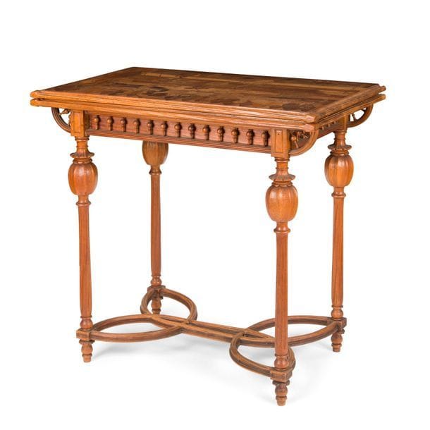 ÉMILE GALLÉ (1846-1904)
Gardez les cœurs qu’avez gagnés, le modèle créé en [1895], variante du modèle présenté à l’Exposition Universelle Paris 1900
Rare table à jeu parlante, à plateau portefeuille, en noyer mouluré, nervuré et sculpté. Les quatre jambages reçoivent un motif de pavot en partie haute et sont réunis par une entretoise en X et H croisés. La ceinture est aux motifs de balustres sur tout son pourtour et se prolonge en arcs de cercle. Le dessus est au décor de chardons et de cardères en marquèterie de bois précieux et indigènes et reçoit la maxime titre également en marquèterie. Le plateau portefeuille s’ouvre sur un intérieur accueillant un tapis de jeu. Circa 1895/1900. Décollements à l’entretoise, manques et soulèvements à la marquèterie, tapis de jeu remplacé, accidents et manques épars. Signée et située GALLÉ à Nancy en marquèterie sur le dessus. 
Table fermée : 75 x 80 x 45,5 cm - Table ouverte : 72,5 x 80 x 90 cm

Provenance :
- Collection d’un grand marchand d’art du début du XXe siècle
- Par descendance

Exposition et musée :
Musée d’Orsay, Paris – Une table à jeu identique conservée dans les collections du musée sous le numéro d’inventaire OAO 494.

Bibliographie :
- Gallé – Catalogue de l’exposition organisée au musée du Luxembourg du 29 novembre 1985 au 2 février 1986, Éditions RMN, Paris, 1985. Un modèle identique (conservé au Musée d’Orsay) reproduit page 267 et largement décrit pages 267 et 268 sous le numéro 156 du catalogue.
- L’École de Nancy – Art nouveau et industries d’art – Catalogue de l’exposition organisée aux galeries Poirel à Nancy du 24 avril au 26 juillet 1999, Éditions RMN et Ville de Nancy, 1999. Légère variante reproduite page 308 sous le numéro 155 du catalogue.
- Gallé furniture - Alastair Duncan et Georges de Bartha, Antique Collectors’ Club, Woodbridge, 2012. Modèle identique reproduit sur la planche 1 de la page 130.