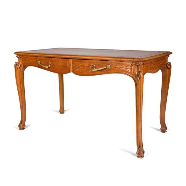 TRAVAIL D’ÉPOQUE ART NOUVEAU
Bureau plat, en noyer sculpté et mouluré, présentant un entablement mouvementé et ouvrant par deux tiroirs en ceinture. La ceinture, les façades de tiroir et les pieds galbés sont aux motifs naturalistes richement sculptés. Les prises naturalistes en bronze d’origine. Circa 1900. Le dessus gainé à neuf de cuir. 76 x 130 x 70 cm