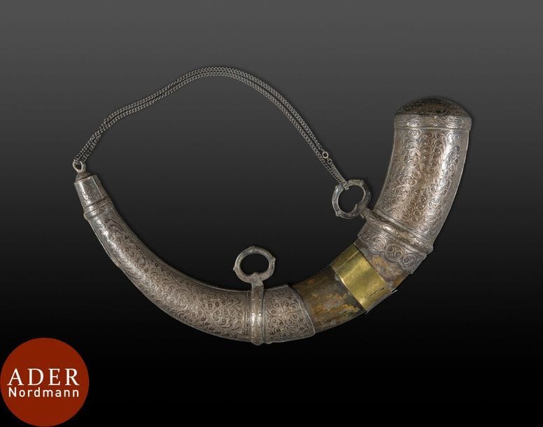 Poire à poudre, Maroc fin XIXe siècle
Poire à poudre en corne garnie de plaques de métal doré et repoussé sur une face, ciselé de volutes sur l’autre. Munie de deux anneaux de suspension et d’une chaîne métallique.
L. : 32 cm
État : une bague de métal fendillée.

A horn powder flask, Morocco, late 19th century