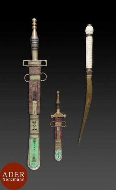 Un poignard et deux couteaux touaregs, Nord du Niger, région d’Agadez, XIXe siècle 
Lames droites, l’une gravée d’une Croix du Sud, fourreaux bout rond cuir brun et teinté en vert (découpé), nielle sur manches. Couteau lame courbe en laiton, manche en os gravé de croisillons.
L. : 23,7, 40,5 et 51 cm
État : oxydations du laiton (petit couteau), décollement du cuir (grand couteau).
On y joint : poignard koumiya, Maroc, fin XIXe siècle. Lame courbe en acier, manche en bois garni de plaques de métal gravé, pommeau surmonté d’un ornement métallique. Fourreau recouvert de plaques de métal à décor gravé d’arabesques. Muni de deux anneaux d’attache latéraux.
L. : 42 cm
État : une plaquette de métal décollée.

A dagger and two touareg knives, North Niger, Agadez region, 19th century