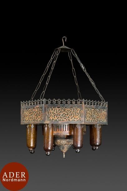 Lampe suspendue en cuivre et verre, Proche-Orient, début XXe siècle
Suspension de forme octogonale, constituée de plaques de cuivre ajouré d’arabesques florales et couronnées d’une frise de merlons.
A la base, dôme inversé ajouré et ciselé entouré de huit lumières (avec leur cylindre de verre brun). Avec quatre chaînes de suspension.
Dim. : 45x45 cm, H. (sans la chaîne) : 32 cm

A copper hanging lamp, Near East, early 20th century