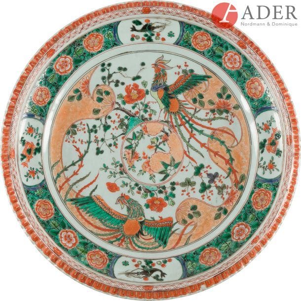 CHINE, Compagnie des Indes - 
Époque KANGXI (1662 - 1722)
Grand plat à bord côtelé en porcelaine décorée en émaux polychromes de la famille verte de deux phénix aux ailes déployés entourant un médaillon orné d’un oiseau, le bord orné de quatre réserves de poissons et écrevisses sur fond de pivoines. (Égrenures).
Diam. : 37,5 cm