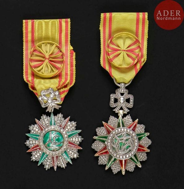 FRANCE - TUNISIE
ORDRE DU NICHAN IFTIKHAR, créé en 1835.
Ensemble de 5 pièces comprenant?:
Deux étoiles d’officier :
- de fabrication tunisienne, au monogramme d’Ali Bey (1992-1902), argent et émail (éclats). 68?x?47?mm - Poids brut?: 33?g
- de belle fabrication française au monogramme de Mohamed El Naceur (1906-1922) en argent, les rayons doublés d’or et émail (éclats et petits coups).
Rubans à rosette. 70?x?47?mm - Poids brut?: 43?g
On y joint trois miniatures en argent, vermeil et émail, une d’officier du Nichan Iftikhar, une d’officier de l’ordre du Ouissam Alaouite et une de chevalier de l’étoile noire du Bénin. Poids brut?: 5,5?g
T.B. à T.T.B. 