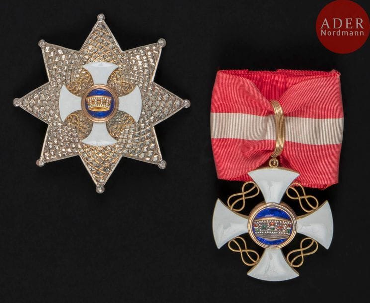 ITALIE
ORDRE DE LA COURONNE D’ITALIE, créé en 1868.
Ensemble de grand officier :
- croix en or et émail (infimes cheveux). Fort anneau strié. Cravate
55?x?50?mm - Poids brut : 18?g
- plaque. Argent travaillé à pointes de diamant, centre en or ciselé et émail.
Revers à attache basculante. Poinçons «?925?» et «?38?» au faisceau de licteur. Marque du fabricant Gardino.
76?mm - Poids brut : 56?g
Dans son écrin au chiffre de Victor Emmanuel de la Maison Gardino, successeur de Cravanzola.
SUP. 