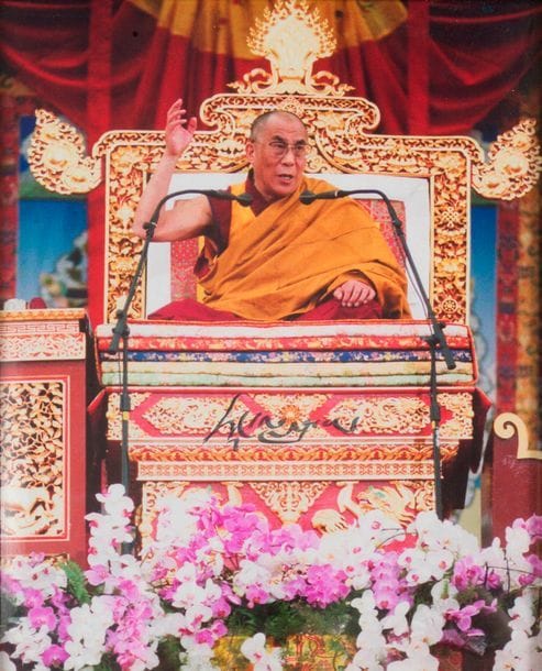 Tenzin Gyastso, DALAI LAMA (né 1935) quatorzième Dalaï Lama, chef du Bouddhisme Tibétain, chassé du Tibet par la Chine. Photographie signée ; 27 x 34 cm en couleurs (encadrée).

   Photographie dédicacée en son milieu, représentant le Dalaï Lama devant un micro lors de l’une de ses conférences, assis en tailleur sur son trône.
