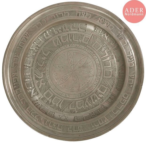 [PESSAH] Plat de Seder 
Assiette en étain portant des poinçons anciens. Gravé et ciselé ultérieurement. 
Écriture de style oriental. 
Sur l’aile, sont inscrits en hébreu, les étapes traditionnelles de la soirée de Pessah. Sur le marli les 3 patriarches et les 4 matriarches. Sur le bassin, d’une écriture et d’un travail moins sophistiqué, sont donnés le nom du graveur, la date hébraïque et une rosace dans laquelle sont inscrits les 12 tribus. 
Diamètre : 43 cm 
Une réparation sur l’aile. Date hébraïque non déchiffrée.




Mots clés : {CR}judaïca, juif, juive, hébreux, rabbins, jewish, torah, hebrew, hebraica,, judaisme, synagogue, sionisme, pessah, pessach, haggada, haggadah, hagada, hagadah, passover, menora, menorah, hannuka, hannuca, hannoucca, hanouccah, torah, juden, israélite, Israël, antisemitism, antisémitisme, dreyfus, meguila, sepharade, sefarad, ketouba