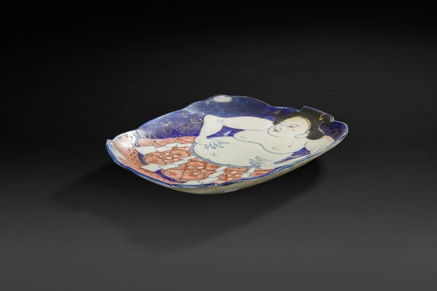 JAPON, Fours de Satsuma - XXe siècle
Plat en faïence de satsuma émaillée polychrome sur fond bleu poudré d’un sumo. (Restaurations). 
L : 26, 5 cm