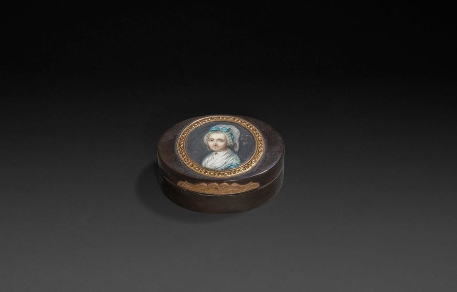 École française du XVIIIe siècle
Femme coiffée d’un bonnet de mousseline à nœud turquoise, robe turquoise et foulard blanc, une croix suspendue à son tour du cou en perles.
Miniature sur ivoire, époque Louis XVI, à vue diam. 3,8 cm, cerclée d’or de deux couleurs sur le couvercle d’une boîte du XVIIIe siècle en écaille mouchetée montée à charnière en or , ovale 5,1 x 6,8 cm x 2,5 cm.
Poinçons sur la charnière dont tête d’homme
Poids brut : 48,20 gr
(petites moisissures à droite)