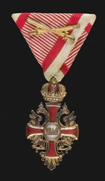 EMPIRE D’AUTRICHE 
ORDRE DE FRANÇOIS JOSEPH, créé en 1849.
Croix de chevalier à titre militaire, fabrication de guerre. 
En bronze doré et émail (petits éclats). Poinçon de l’orfèvre BÖHM à Vienne. Ruban triangulaire à motif aux glaives entrecroisés. 
53 x 30 mm - Poids brut : 2,9 g 
Dans son écrin frappé « F.J.O ». 
T.T.B.