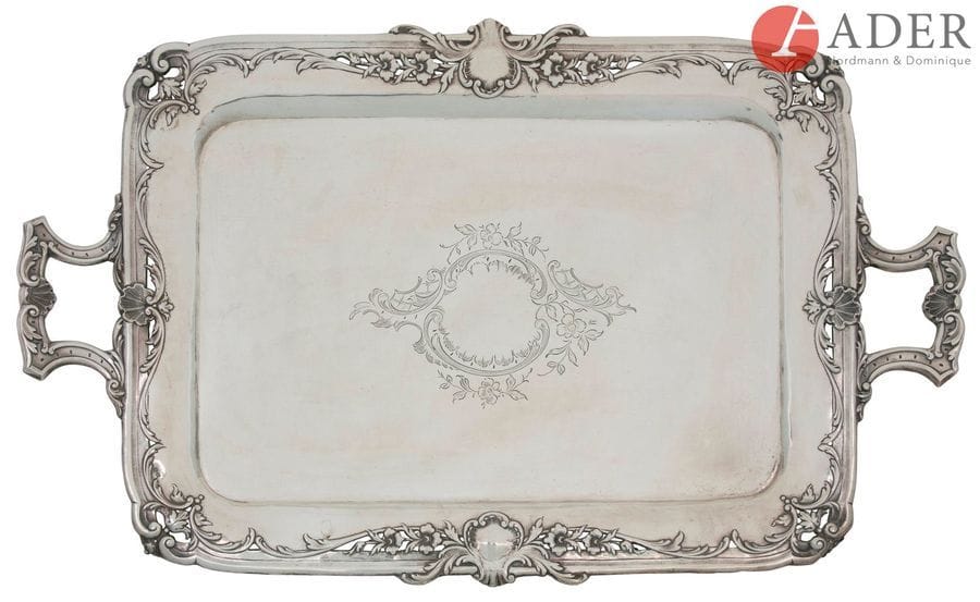 PORTO, 1886 - 1938
Grand plateau à deux anses en argent (833 ‰) gravé d’un médaillon fleuri en son centre, la bordure repercée de coquilles, d’agrafes et de fleurs stylisées.
Poids net : 2455 g - longueur aux anses : 67,5 cm largeur : 43 cm