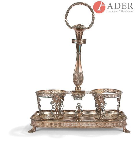 PARIS, 1798 - 1809
Monture d’huilier-vinaigrier sur plateau en argent reposant sur une base rectangulaire dont les supports figurent deux pieds côte à côte à la mode égyptienne, les porte-carafes estampés de visages féminins, la prise figurant une corbeille de fruits. Manquent les carafes.
Poinçon de garantie des orfèvres
Poids net : 703,80 g - hauteur : 30 cm