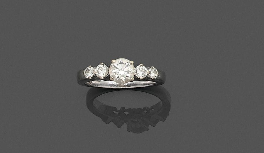 Bague en or gris 18K (750), ornée d'un diamant rond épaulé de 4 diamants ronds plus petits. Tour de doigt : 54. Poids brut : 5,9 g