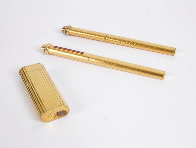 CARTIER. Lot de deux stylos bille et un briquet en métal doré guilloché. Signés.
