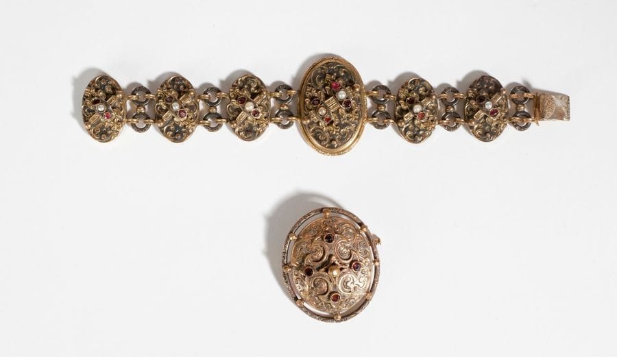 Bracelet en métal, articulé de motifs ovales à décor moulé sertis de pierres rouges et demi-perles (certaines fausses). Travail du XIXe siècle. Longueur: 18,5 cm environ. On joint une broche en métal, de forme ovale, agrémentée de pierres rouges.