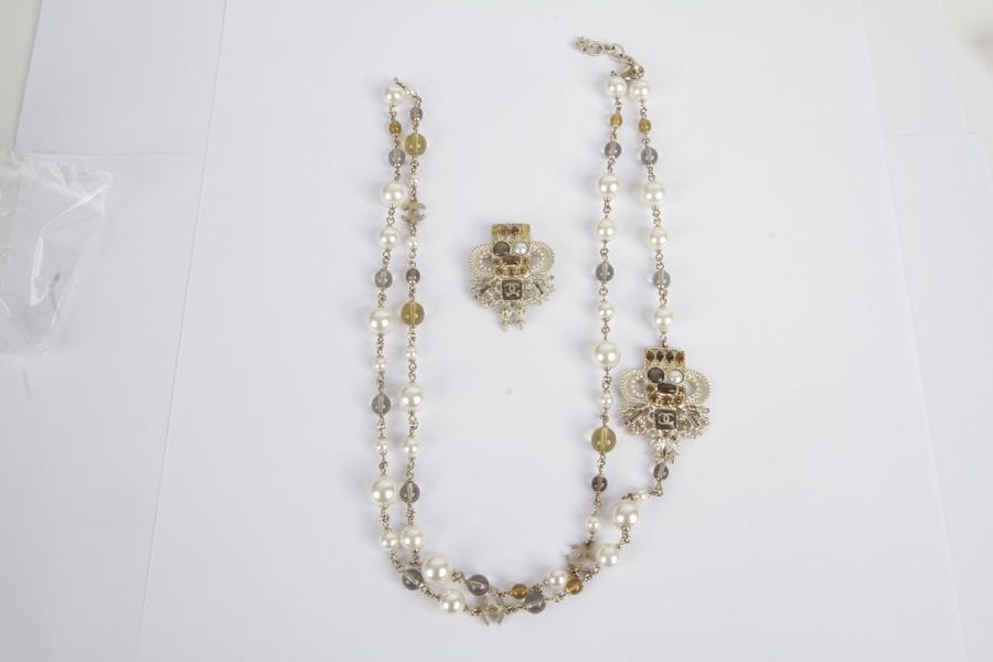 Demi-parure fantaisie agrémentée de perles de verre et de perles imitation, scandées de double C, comprenant un long collier et une broche assortie. Dans sa boîte. Longueur: 110,5 cm environ. Hauteur de la broche: 4,5 cm environ