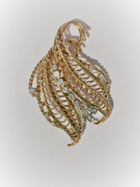 Broche en fils d'or 18K (750) dessinant des feuilles stylisées, agrémentée de diamants ronds sur platine. Travail français des années 1950. Hauteur: 6 cm environ. Poids brut: 16,2 g