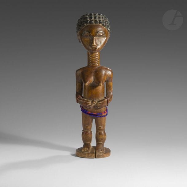 Une statuette féminine au cou annelé, les yeux en demi-lune, les mains sur le ventre et les seins tendus, orné de bracelets de perles. 
Agni, RCI
Bois, belle patine blonde d’usage, pigment, petits accidents et fentes d’ancienneté, restauration au socle (cassé collé).
H. : 32 cm

Provenance :
Ancienne coll. Iba Ndiaye