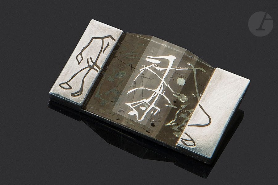 JEAN DESPRÉS (1889-1980) & ÉTIENNE COURNAULT (1891-1948)
Sans titre, circa 1930
Exceptionnelle broche moderniste en argent.
La partie centrale, en glace peinte et travaillée dans son épaisseur, est enchâssée sur une platine en argent comprenant deux parties latérales poursuivant l’œuvre centrale par des motifs en laque noire.
Porte le poinçon de Maître Orfèvre au revers et celui de garantie sur la tranche.
Hauteur : 3 cm – Longueur : 5,2 cm 
Poids brut : 41,43 g

Provenance :
- M. & Mme X., Paris et Courson-les-Carrières, intime de Jean Després. Œuvre acquise directement auprès de l’artiste.
- Œuvre restée dans la descendance des précédents par voie de succession.

Bibliographie et œuvres en rapport :
- Jean Després, maestro orafo tra art deco e avanguardie - Melissa Gabardi, Idea Books, Milano, 1999. Des œuvres de collaboration entre Jean Després et Étienne Cournault reproduites pages 44 à 53.
- Jean Després : bijoutier et orfèvre en Art Déco et modernité - Melissa Gabardi, Norma Éditions & Musée des Arts Décoratifs, Paris, 2009. Œuvre à la monture identique présentant une autre glace peinte d’Étienne Cournault reproduite page 42. 