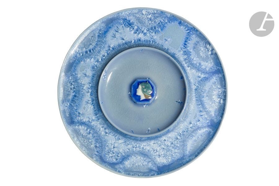 TAXILE DOAT (1851-1939)
Portrait de profil, circa 1904
Plat circulaire à l’aile et le centre en cuvette.
Épreuve en porcelaine émaillée ; l’aile traitée d’une riche irisation venant, de façon éparse, déborder sur la partie centrale.
Le centre reçoit le médaillon titre polychrome réalisé en pâte sur pâte.
Signé et situé DOAT Sèvres au revers.
Diamètre : 19,5 cm

Bibliographie et œuvres en rapport :
Art et Décoration, septembre 1904 – Œuvres à rapprocher reproduites pages 80 et 82.
