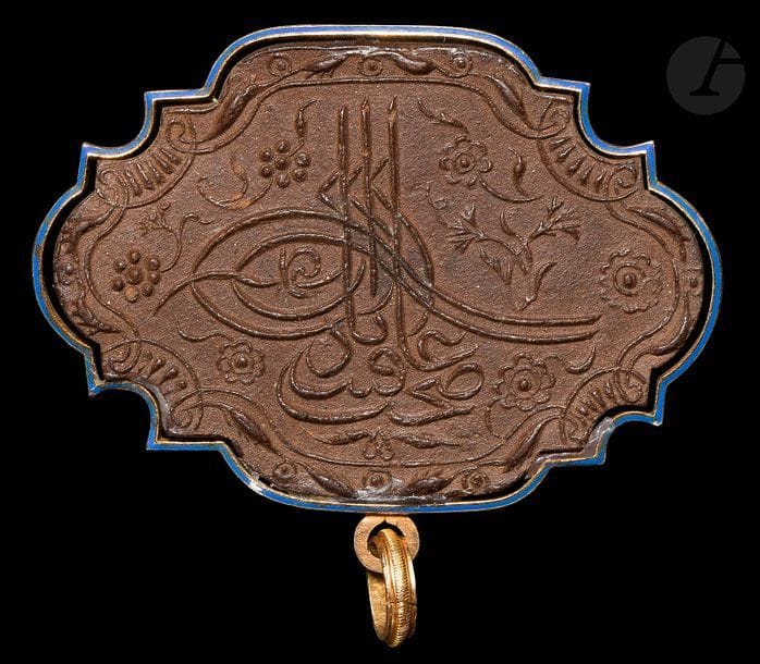 Tablette d’ambre gris, misk-i amber, Turquie ottomane, XVIIIe siècle
Plaquette d’ambre gris à contour chantourné ornée d’un décor moulé : sur une face, pseudo tughra constituée non des noms d’un sultan mais des mots : « ‘afiyet » et « sahet », « bien-être » et « santé » entourée de fleurs, œillets et rosettes et encadrée de tiges feuillues enroulées. Sur l’autre face, deux vers poétiques inscrits dans des cartouches horizontaux en turc ottoman et encadrés des mots « santé » et « bien-être » et de tiges végétales. Monture métallique en pendentif.
Hauteur : 4,5 cm ; Longueur : 6,4 cm

Nombreuses légendes se sont développées autour de l’ambre gris, rendant cette matière toujours plus mystérieuse : si les Chinois, 2000 ans avant JC, le dénommaient « parfum de la bave de dragon », Avicenne pensait que l’ambre gris provenait d’une fontaine sous-marine, sans doute inspiré par les Mille et Une Nuits où Sindbad le marin voit jaillir de l’ambre d’une source avant qu’il ne soit avalé par des monstres marins… Il s’agit en réalité d’une sécrétion qui se forme dans l’estomac ou les intestins du cachalot et est rejetée ensuite par les voies naturelles de l’animal. Fossilisé par le temps, le sel de mer et le soleil, il est repêché à la surface de l’eau ou s’échoue sur les plages où il est ramassé par blocs. Depuis la plus Haute Antiquité, les hommes lui trouvent des vertus médicinales mais aussi odoriférantes et aphrodisiaques. D’un point de vue médical, il a longtemps été utilisé comme remède à l’asthme et à l’épilepsie. Les Arabes l’utilisaient aussi pour soigner les articulations, les troubles digestifs, le cœur et le cerveau. Arrivé en Europe au Moyen-Âge à prix d’or, il était porté en collier et respiré pour renforcer ses défenses immunitaires contre les fléaux sanitaires tels que la peste. Puissant fixateur d’odeurs, l’ambre gris était un composant essentiel des parfums du XXe siècle ; il est aujourd’hui remplacé par des accords de synthèse. L’effet aphrodisiaque 