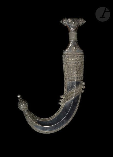 Poignard Djambiya, Yémen, XIXe siècle
Monture en corne rehaussée de garnitures en argent sur la face et le pommeau à décor perlé et filigrané. Lame courbe à double tranchant renforcée d’une nervure médiane, et fort damasquiné d’or de cartouches fleuronnés garnis de rinceaux et d’inscriptions en arabe donnant sur une face le nom du propriétaire : « sahib Malik […] ibn Mustafa », sur l’autre : « ya Muhammad fajl Shafi’in […] » / « gloire aux intercesseurs […] ». Fourreau en bois recouvert de plaques d’argent à décor filigrané et pastillé formant des frises végétales. Anneaux d’attache latéraux et bouterole en dard.
Longueur : 31 cm ; Longueur max avec fourreau : 34,5 cm
État : cabossages, petit trou sur le fourreau, métal noirci, âme de bois mobile.

Apparaît sur la 4e de couverture du livre d’Alain Jacob. Les armes blanches du monde islamique - Les armes de poing, Paris : 1985.


A horn-hilted dagger, djambiya, Yemen, 19th century

Ancienne collection de Monsieur A. Jacob (1942-1988)
Lots de 340 à 351
Alain jacob (1942-88), grand passionné et spécialiste des armes blanches, auteur d’une thèse sur les cimeterres turco-iraniens, travailla au Musée du Louvre et au Musée de l‘Armée avant de devenir rédacteur en chef de la revue d’antiquités ABC, membre fondateur de l’Union Française des Experts, il en devint ensuite vice-président. Il est l’auteur d’une série d’articles très documentés et d’ouvrages de référence sur les armes blanches du monde islamique et de l’Afrique : Armes blanches de l’Afrique Noire, Paris : 1974 ; Les armes blanches du monde islamique, Paris : 1985.