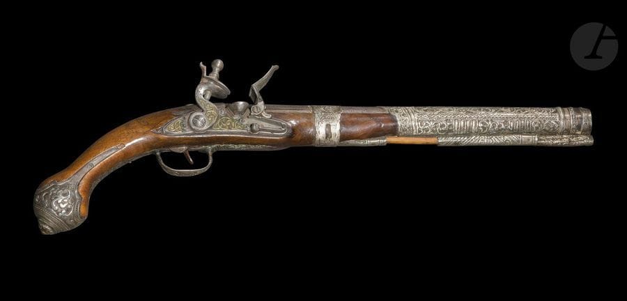 Pistolet à silex, Afrique du Nord ottomane, XIXe siècle
Canon rond à pans sur le dessus, à garnitures et bague d’argent repoussé et gravé d’un décor végétal et géométrique et accueillant la tige de bourre en bois. Platine à silex et chien col de cygne à décor de rinceaux incrustés de laiton.Crosse en bois à long fut à décor gravé sur le dessus, d’une plaque de métal découpé au niveau du tonnerre. Pommeau rond à oreilles en métal à décor moulé et gravé de cercles concentriques et de palmettes reprises sur le pontet. Deux traces de poinçons illisibles sur les oreilles.
Longueur : 51,5 cm
État : silex manquant, quelques traces d’oxydation.

A flintlock pistol, Ottoman North Africa, 19th century

Ancienne collection de Monsieur A. Jacob (1942-1988)
Lots de 340 à 351
Alain jacob (1942-88), grand passionné et spécialiste des armes blanches, auteur d’une thèse sur les cimeterres turco-iraniens, travailla au Musée du Louvre et au Musée de l‘Armée avant de devenir rédacteur en chef de la revue d’antiquités ABC, membre fondateur de l’Union Française des Experts, il en devint ensuite vice-président. Il est l’auteur d’une série d’articles très documentés et d’ouvrages de référence sur les armes blanches du monde islamique et de l’Afrique : Armes blanches de l’Afrique Noire, Paris : 1974 ; Les armes blanches du monde islamique, Paris : 1985.